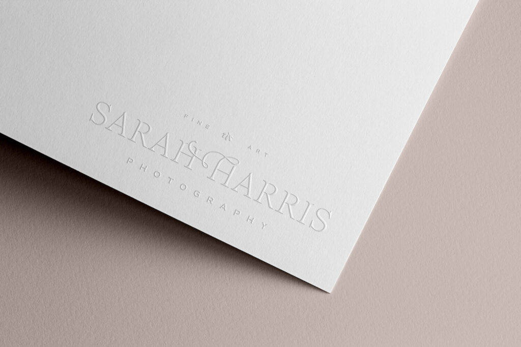 A mockup of the Sarah Harris Photography logo embossed on white paper over a soft pink background.